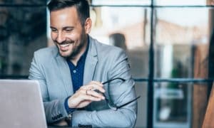 business man in suit smiling at computer with glasses in hand