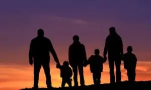 Family standing on hill holding hands while sun is setting