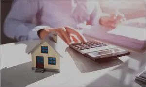 Toy house on table next to person using calculator
