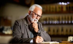 Older man sitting down looking at book holding chin while thinking