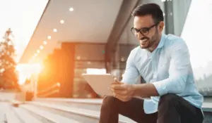 Business man sitting on stairs outside on tablet smiling at sunset
