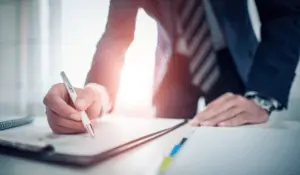 business man leaning over counter writing on a document with a pen - Financial Planning Checklist blog